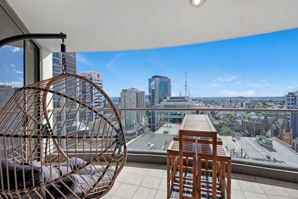 A balcony with a hanging chair, a table, and a city view.