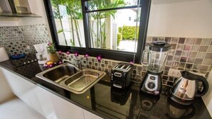 Une cuisine dotée d’un plan de travail noir, d’un évier en acier inoxydable, d’un grille-pain, d’un mixeur et d’une machine à café.