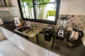 Een keuken met een zwart aanrecht, een RVS spoelbak, een broodrooster, een blender en een koffiezetapparaat.