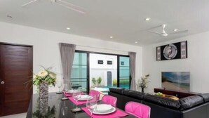 Un salon moderne comprenant un coin repas, un canapé en cuir noir, une table à manger agrémentée de sets de table roses et une grande fenêtre offrant une vue dégagée.