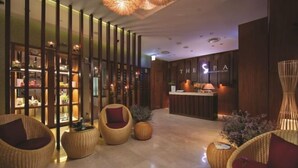 Un espace d’accueil moderne pour un spa, avec un comptoir de réception en bois, des fauteuils en osier et un mur décoratif agrémenté d’étagères.