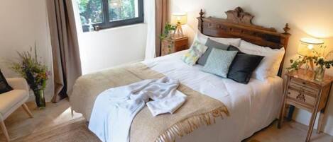 A bedroom with a large bed, two bedside tables with lamps, a wooden headboard, and a window with curtains.