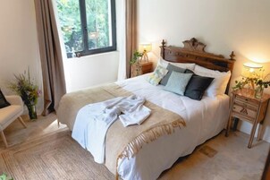 Un dormitorio con una cama grande, dos mesitas de noche con lámparas, un cabecero de madera y una ventana con cortinas.