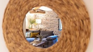 A round mirror with a woven frame reflecting a room with a stone wall, a sofa, and a lamp. - Domaine 20 people with swimming pool, spa and tennis (Saint-Julien-les-Rosiers)