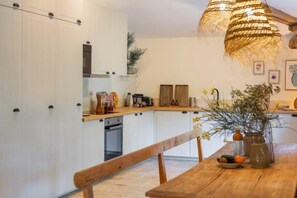 A kitchen with white cabinets, a wooden dining table, and a hanging light fixture. - Domaine 20 people with swimming pool, spa and tennis (Saint-Julien-les-Rosiers)