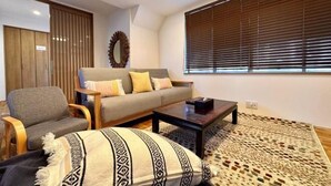 A modern living room with a sofa, armchair, coffee table, and patterned rug. - Haku Wakanayanagi Inn (Kyoto)