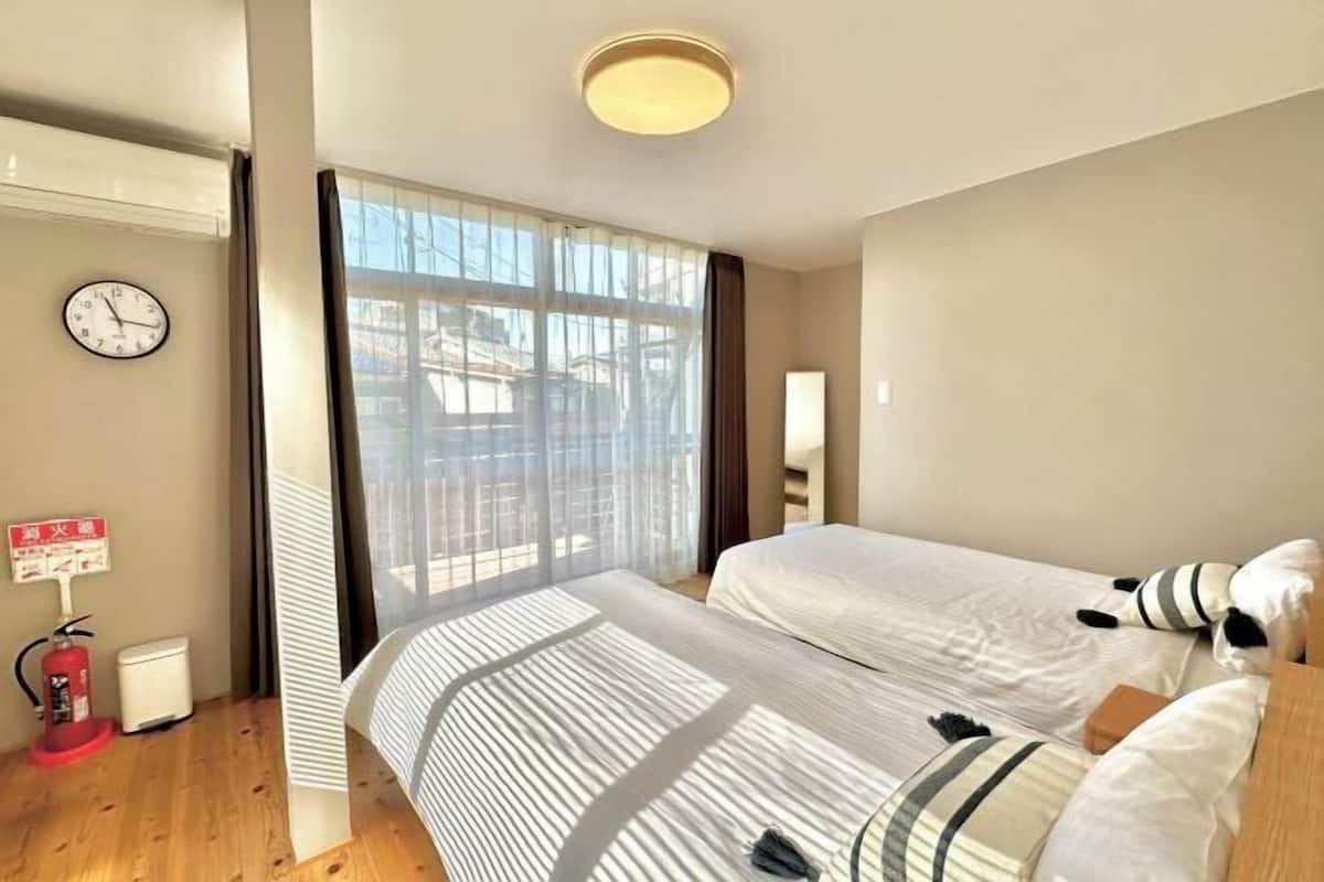 A hotel room with two beds, a clock, a fire extinguisher, and a window with curtains.