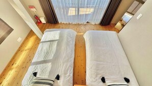 A room with two beds, wooden flooring, a window with curtains, and a visible fire extinguisher. - Haku Wakanayanagi Inn (Kyoto)