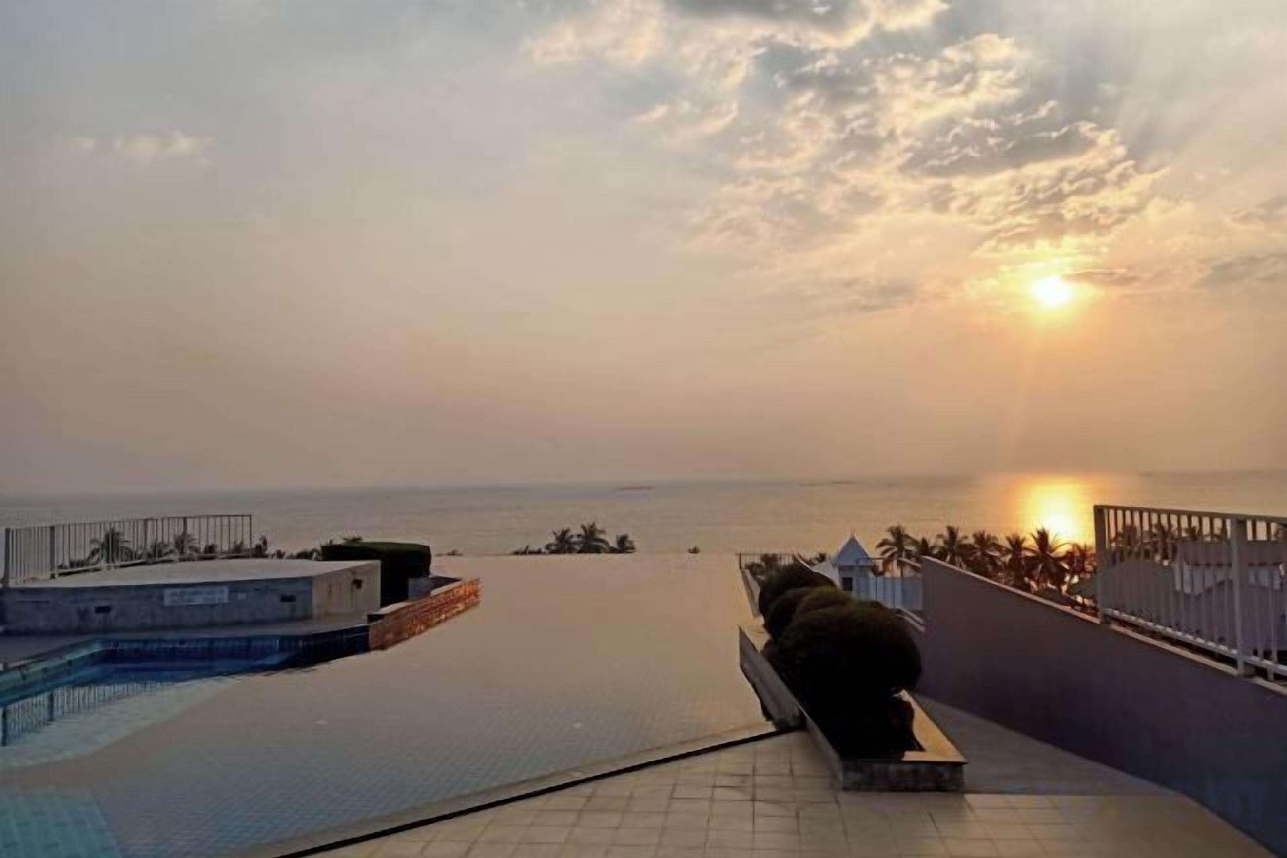 A rooftop pool with a view of the sunset over the ocean.