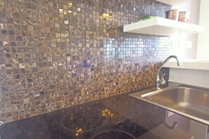 Een keuken met een zwart aanrecht, een roestvrijstalen spoelbak en een mozaïek achterwand.