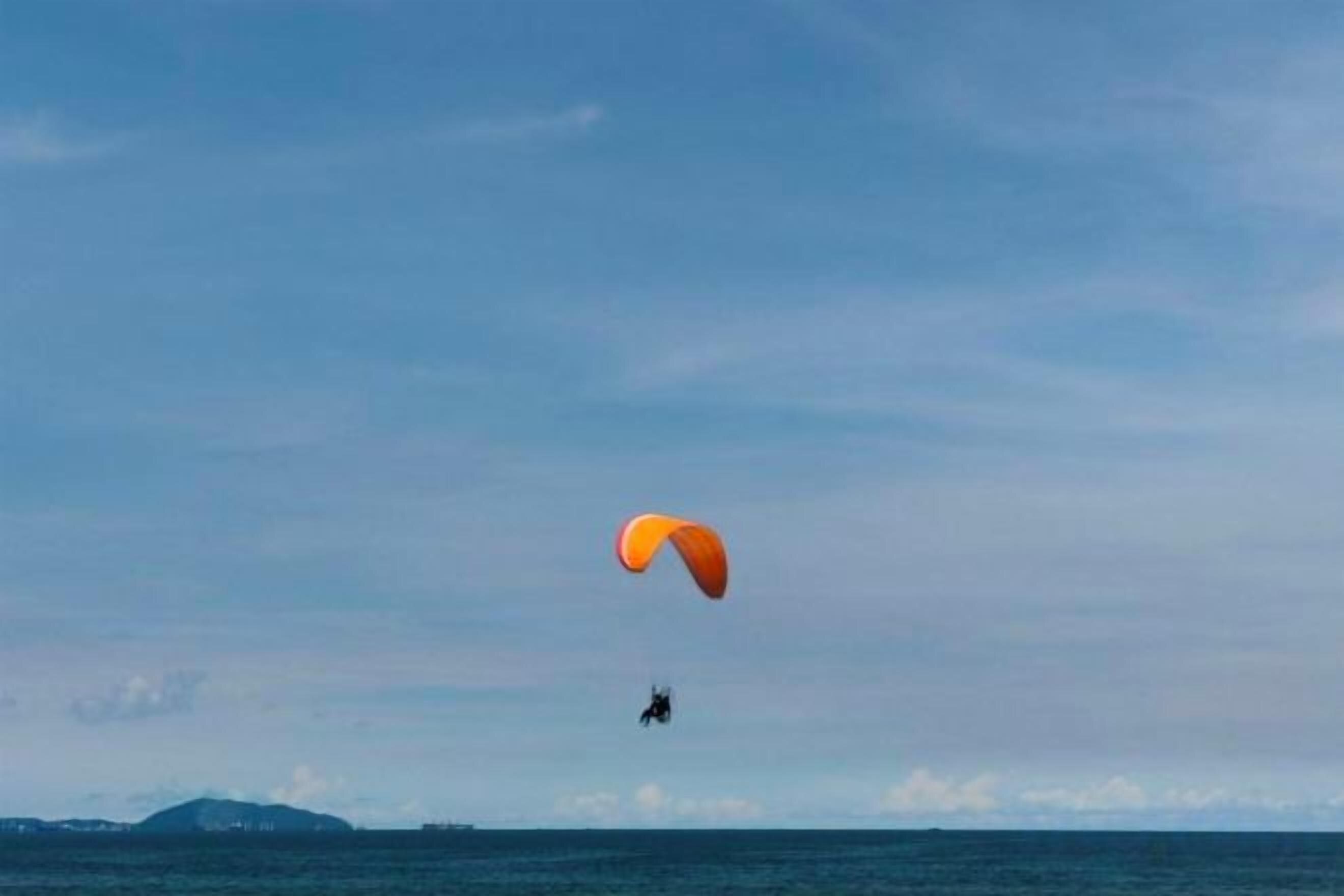 A person paragliding over a body of water with a distant landmass.