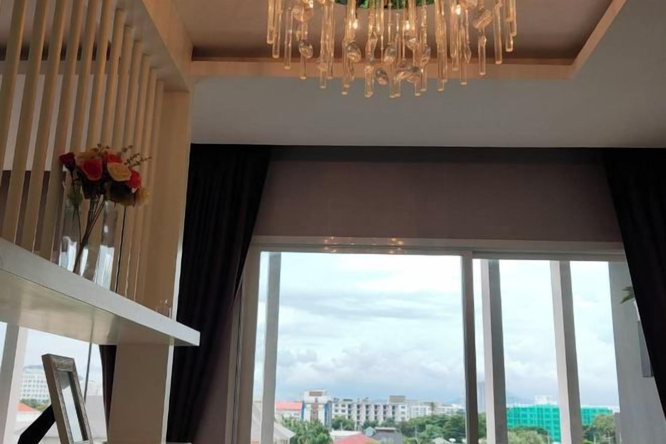 A room with a large window, a modern chandelier, and a view of buildings outside.