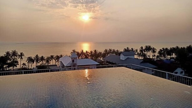 Ein Pool in einer Hotelanlage mit Blick auf einen Sonnenuntergang, Palmen und Strandhütten.