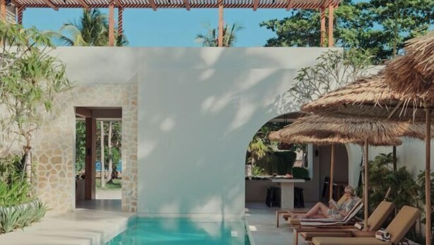 A poolside area with lounge chairs and a thatched umbrella, surrounded by greenery and a stone wall. - Boni Beach Lombok Hotel & Restaurant (West Praya)
