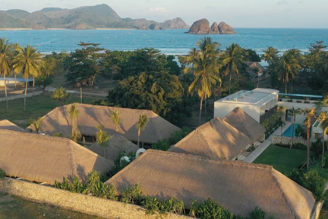 Un resort con cabañas de techo de paja, palmeras y vista al mar.