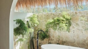 A bathroom with a stone wall, a thatched roof, and lush greenery. - Boni Beach Lombok Hotel & Restaurant (West Praya)