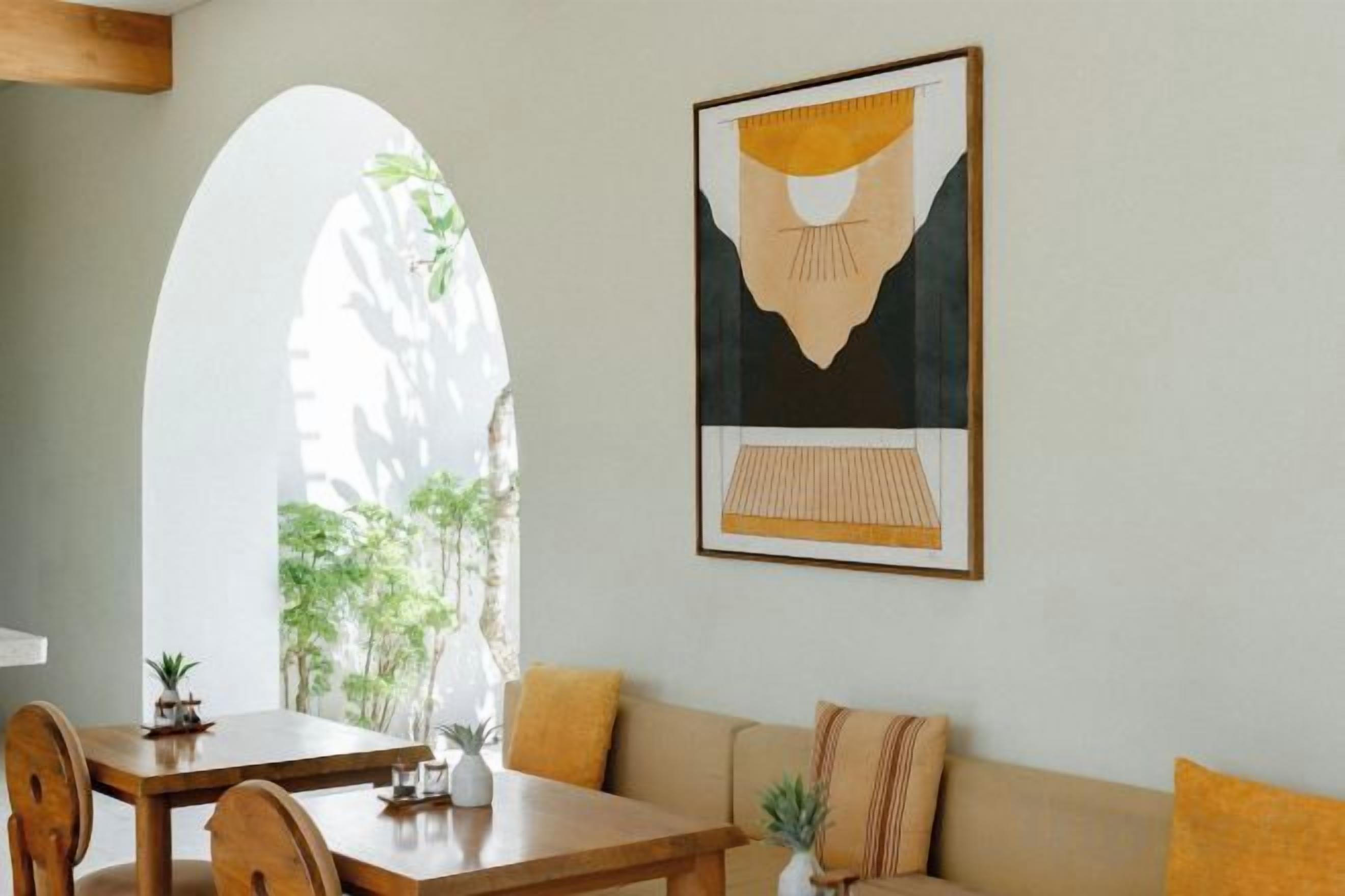 Een eetgedeelte met een tafel, stoelen en een bank. Er hangt een kunstwerk op de muur en een raam met uitzicht op groen.