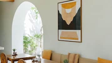 Een eetgedeelte met een tafel, stoelen en een bank. Er hangt een kunstwerk op de muur en een raam met uitzicht op groen.