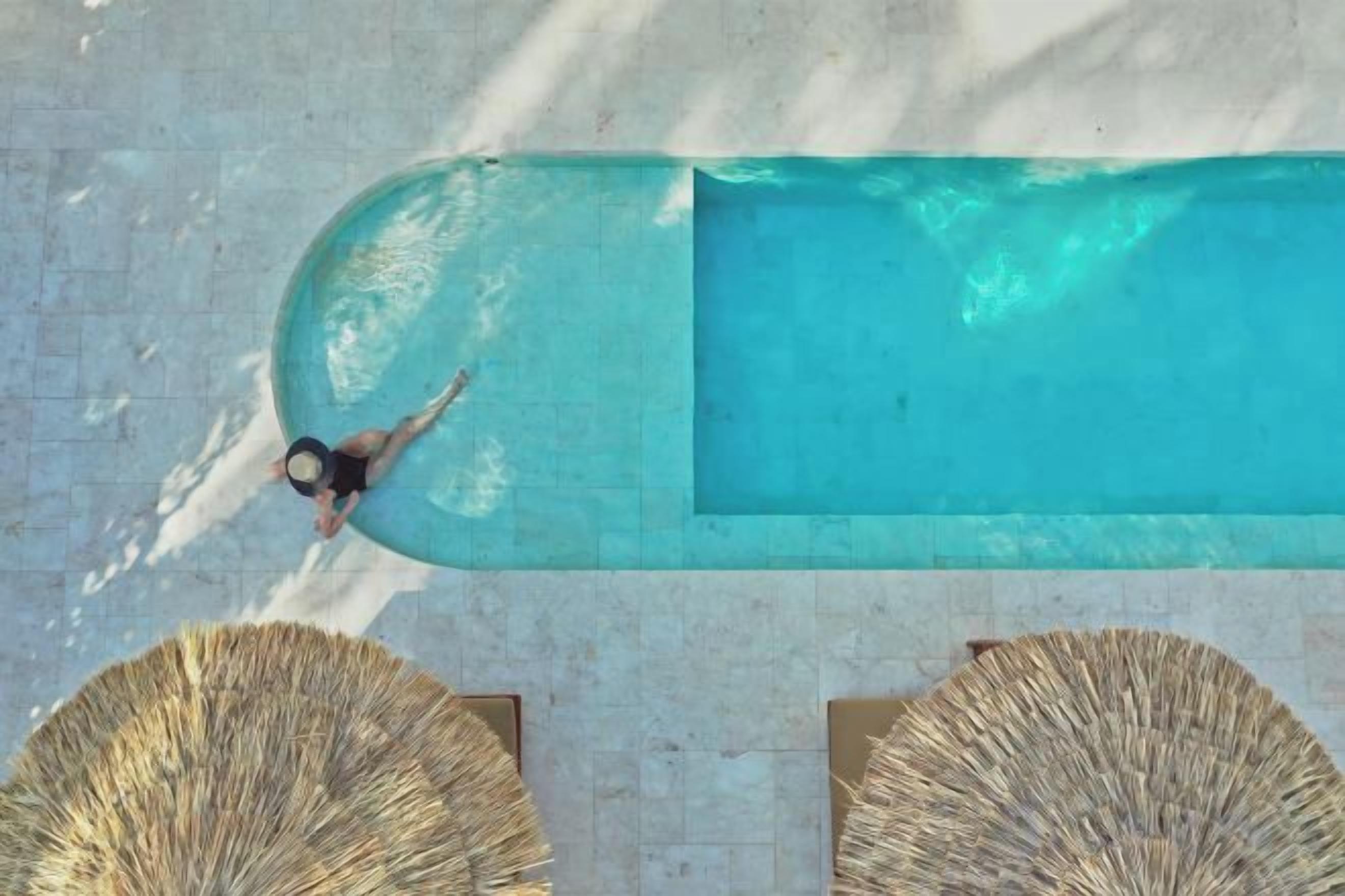 Piscina rectangular con una persona nadando, rodeada de tumbonas.