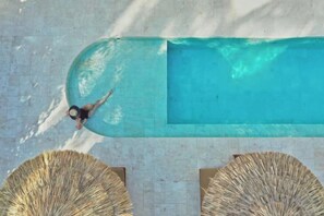 A rectangular swimming pool with a person swimming, surrounded by sun loungers. - Boni Beach Lombok Hotel & Restaurant (West Praya)
