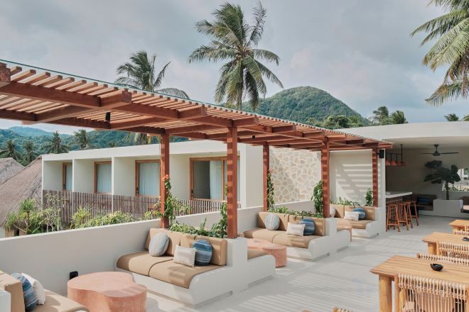 Un lounge en la azotea con mobiliario exterior, una pérgola y vistas a palmeras y montañas.