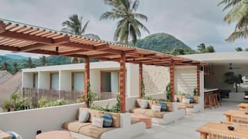 A rooftop lounge with outdoor seating, a pergola, and a view of palm trees and mountains.
