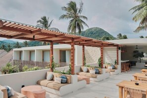 Un lounge en la azotea con mobiliario exterior, una pérgola y vistas a palmeras y montañas.
