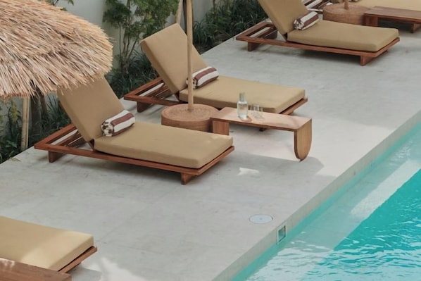 Un espace aménagé au bord de la piscine, avec des chaises longues et un parasol en chaume.