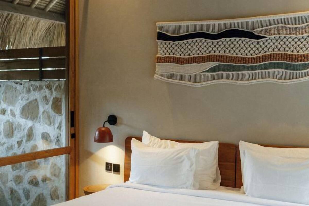 Ein Bett mit weißen Leinentüchern, einem Holzkopfteil und einer Wandlampe.
