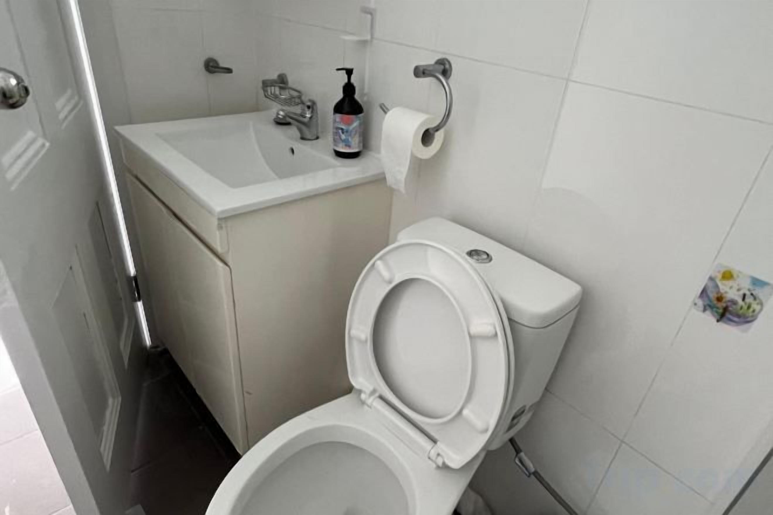 A white toilet with a closed seat, a white sink with a soap dispenser, and a toilet paper holder on the wall.