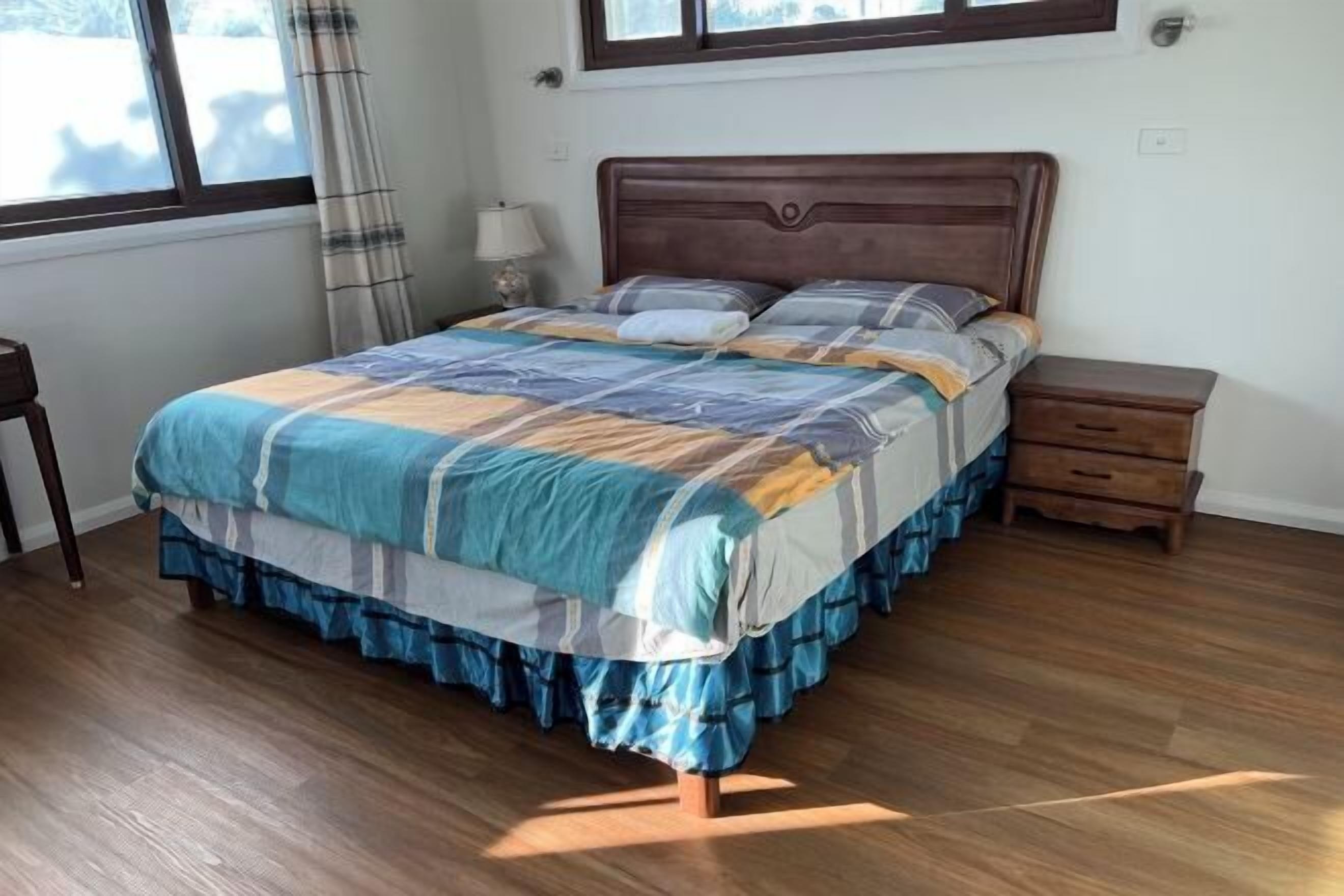 A bedroom with a wooden bed, a nightstand, a lamp, and a window with curtains.