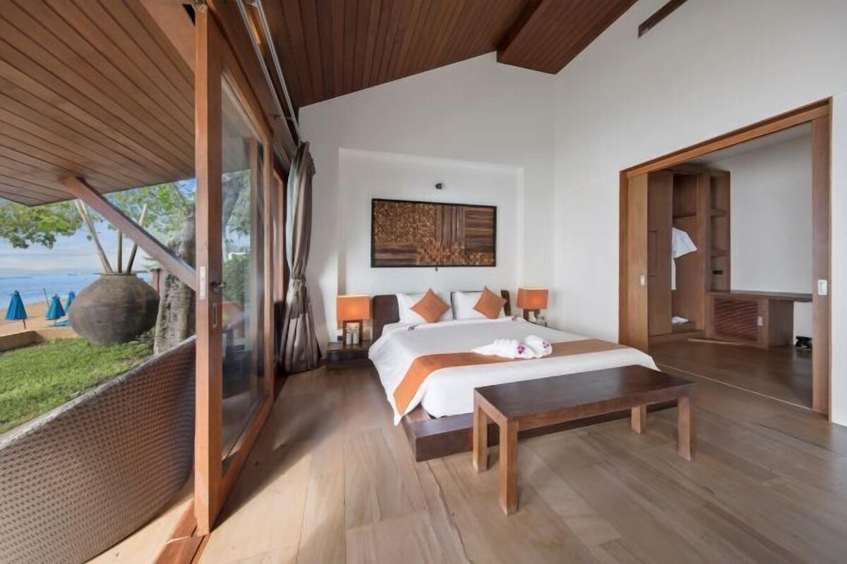 A modern hotel room with a large bed, wooden flooring, a view of the sea, and a large artwork on the wall.