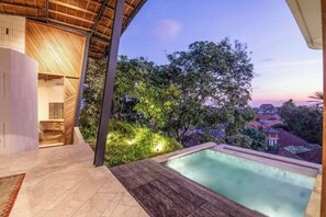A modern hotel room with a pool, a wooden ceiling, and a view of the surrounding greenery and buildings. - BAz Penthouse (Bali)