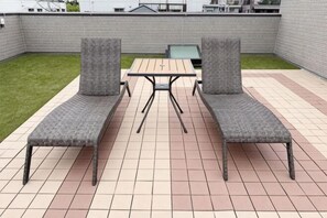 An outdoor patio with two grey cushioned chairs and a table, surrounded by a tiled floor and a low brick wall. - FUKUNOSO TOUJIN (Fukuoka)