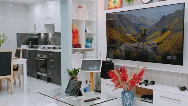A modern kitchen with white cabinetry, a built-in oven, and a large flat-screen TV displaying a mountainous landscape. - Min Su Rooms (Stanwell)