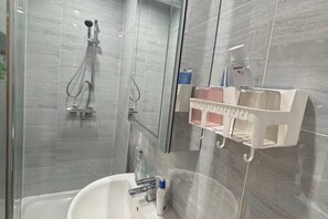 Een moderne badkamer met een douchecabine van glas, een witte wastafel en een spiegel.