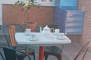 A table set with white teacups, a teapot, and saucers on a white table, with a potted plant and chairs around it. - Min Su Rooms (Stanwell)