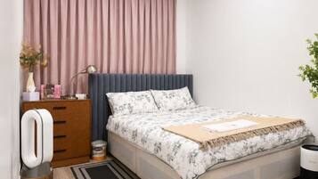 Quarto com cama, mesa de cabeceira, cômoda, luminária, planta e janela com cortinas.
