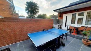 A ping pong table in a backyard with a brick wall, a potted plant, and a house in the background. - Min Su Rooms (Stanwell)