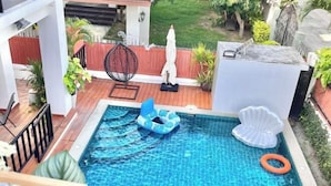 A swimming pool with a wooden deck, a lounge chair, and a white shell float. - Casa jomtien village Pattaya Sea Sky Pool Villa (Pattaya)