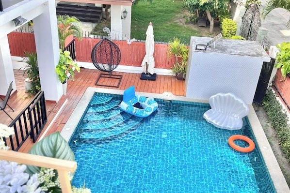 A swimming pool with a blue inflatable lounge, a white shell-shaped float, and an orange ring float.