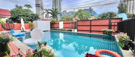 A swimming pool with a red inflatable ring, surrounded by a fence and various plants.
