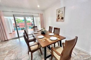 A dining area with a long table, chairs, and a view through a glass door to an outdoor space. - Casa jomtien village Pattaya Sea Sky Pool Villa (Pattaya)