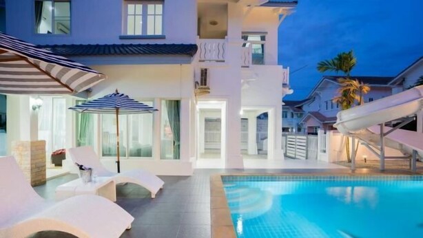 A pool area with lounge chairs and umbrellas, a water slide, and a building with balconies. - Baba beach (Pattaya)