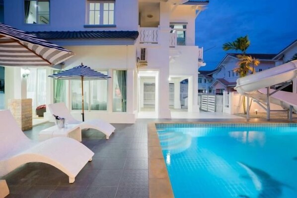 A swimming pool with lounge chairs and umbrellas, a slide, and a building with multiple balconies. - Baba beach (Pattaya)