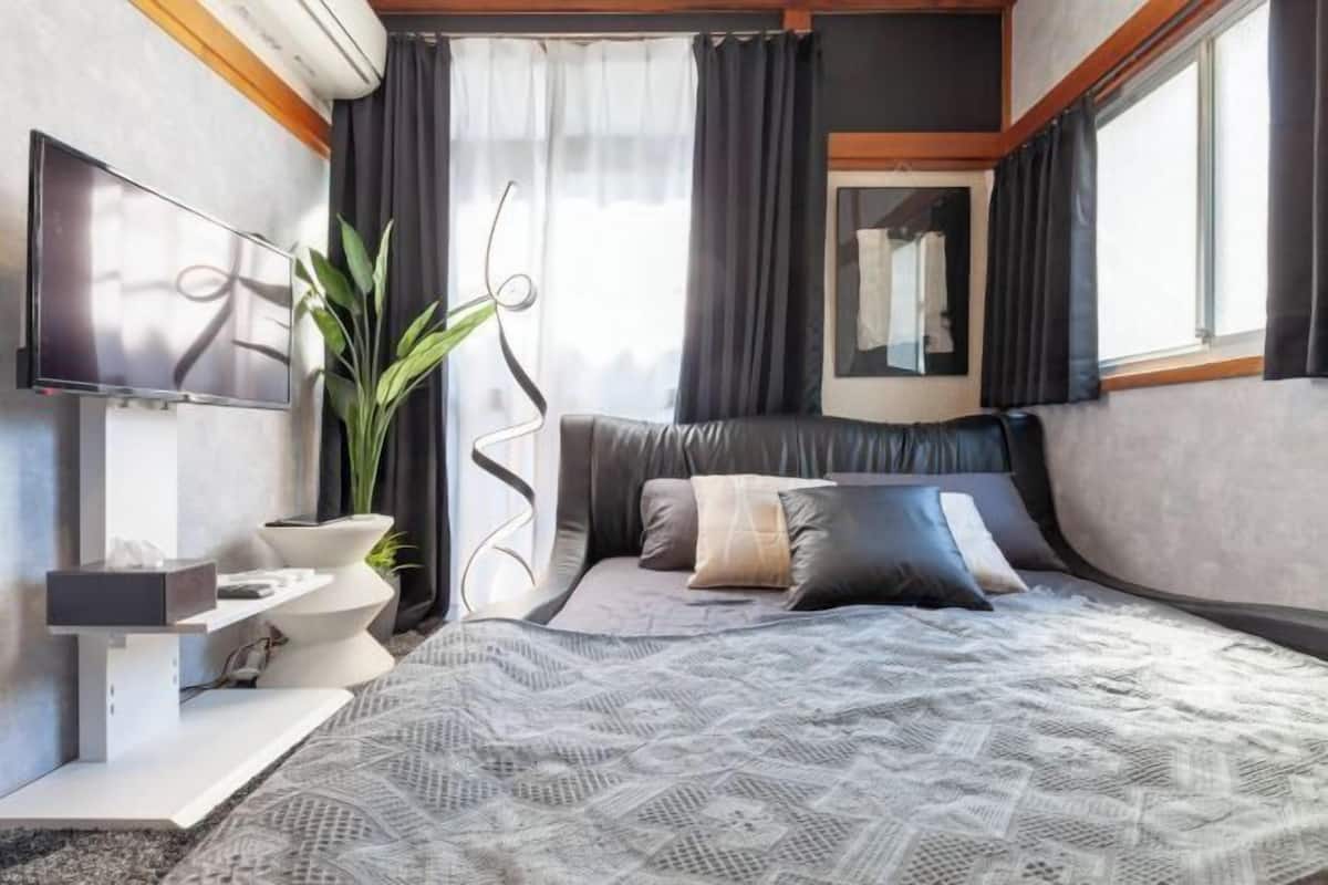 A modern bedroom with a bed, a TV, a plant, and a window with curtains.