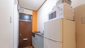 A compact kitchen with a refrigerator, microwave, and a wooden door. - Shiinamachi house (Tokyo)