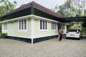 A single-story house with a tiled roof, a covered porch, and a car parked in front. - Riverside Homestay by Nature (Idukki)
