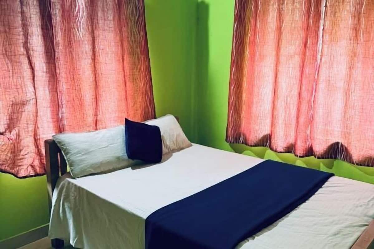 A bed with white and dark blue bedding, a pillow, and a green wall.