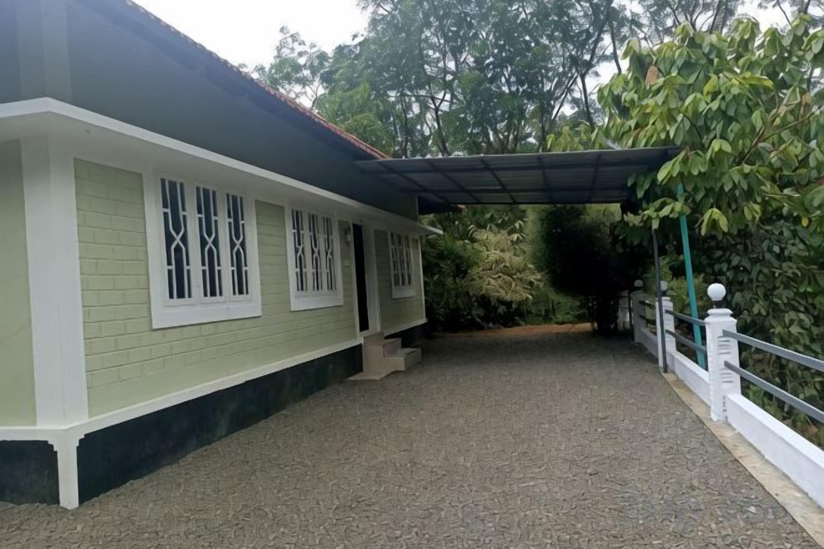 Un edificio con un patio cubierto, un camino de entrada de grava y una barandilla blanca.